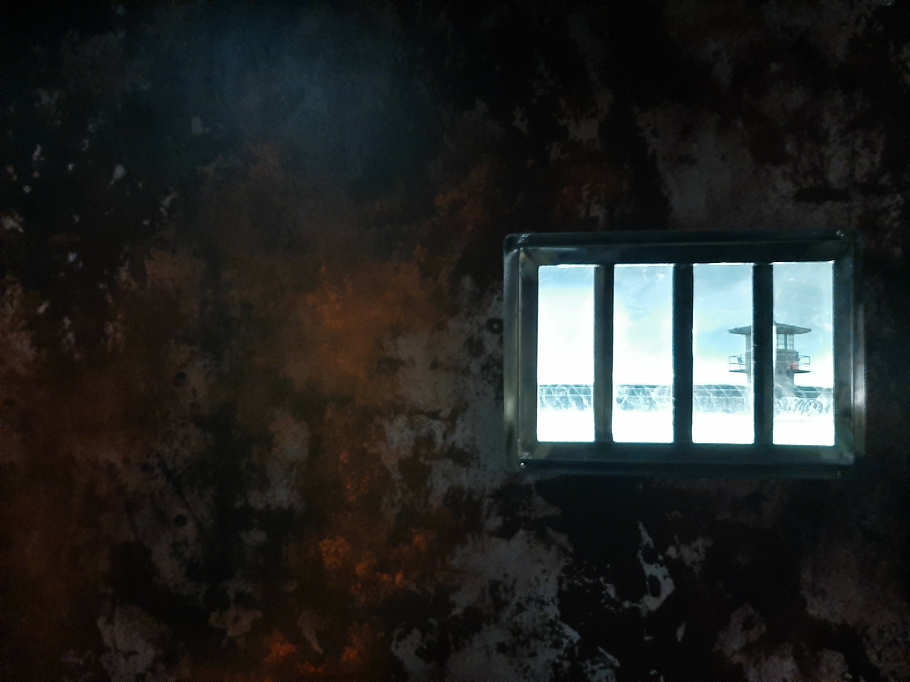 Intérieur d'une cellule avec fenêtre à barreaux illuminée, évoquant les activités à faire lors d'une sortie ludique chez Prison Island 77 en Seine-et-Marne, rappelant l'univers de Fort Boyard, parfait pour les loisirs entre amis ou en famille.