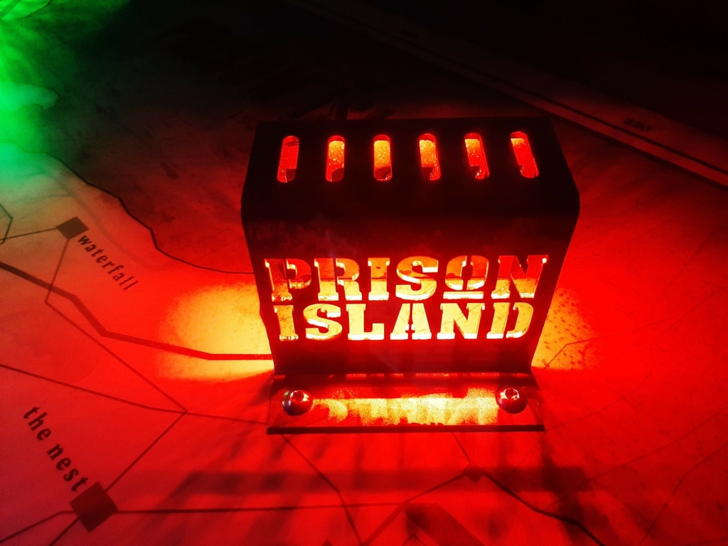 Une porte rouge vif avec le logo "Prison Island" découpé, posée sur une carte, illustrant les activités à faire pour une sortie de loisirs immersive entre amis ou en famille chez Prison Island 77 en Seine-et-Marne, rappelant l'aventure de Fort Boyard.